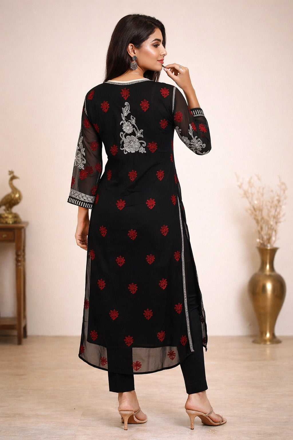 Woman wearing a black traditional outfit with red and white patterns in a minimalistic setting.