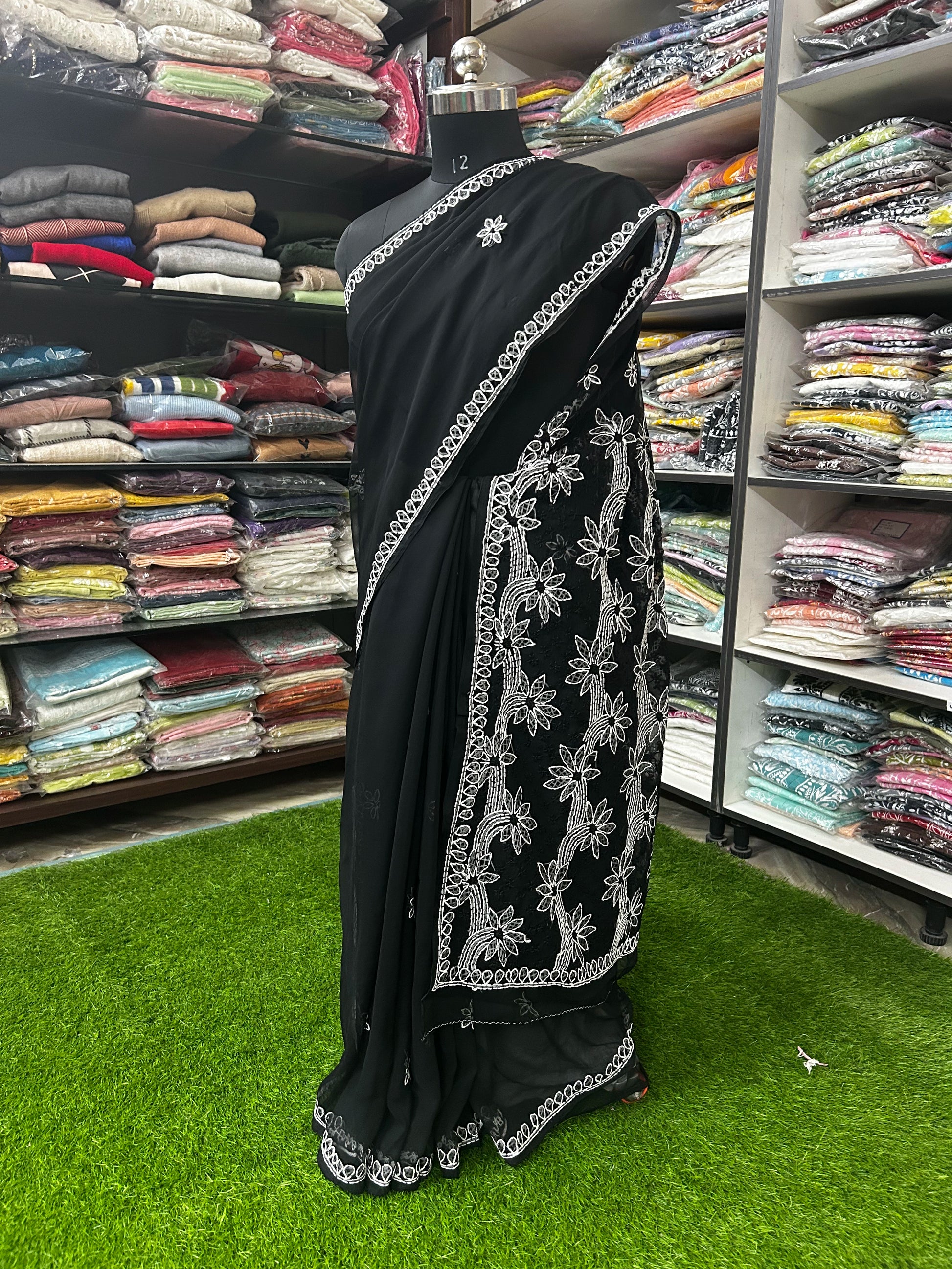Black saree with white embroidery on a mannequin in a fabric store.