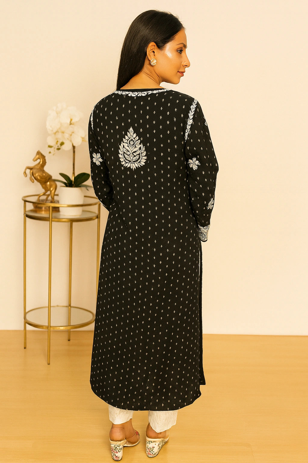 Woman wearing a black kurta with white embroidery and white pants against a beige background