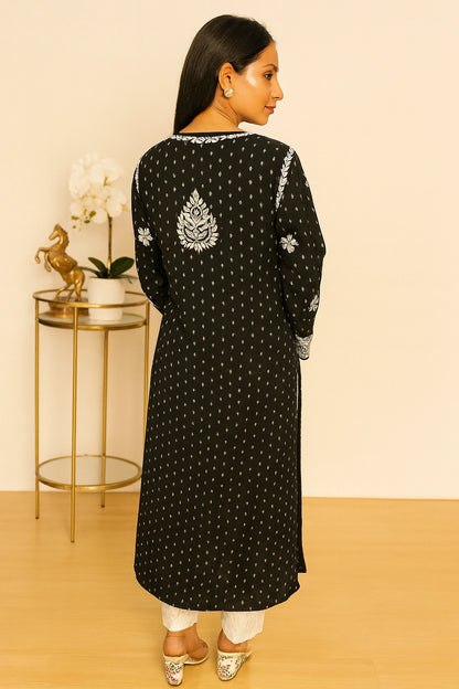 Woman wearing a black kurta with white embroidery and white pants against a beige background