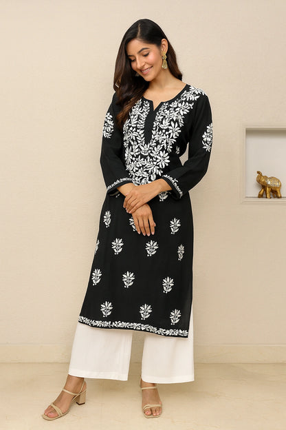 lucknowi chikankari Woman wearing a black and white embroidered kurta with white pants on a beige background