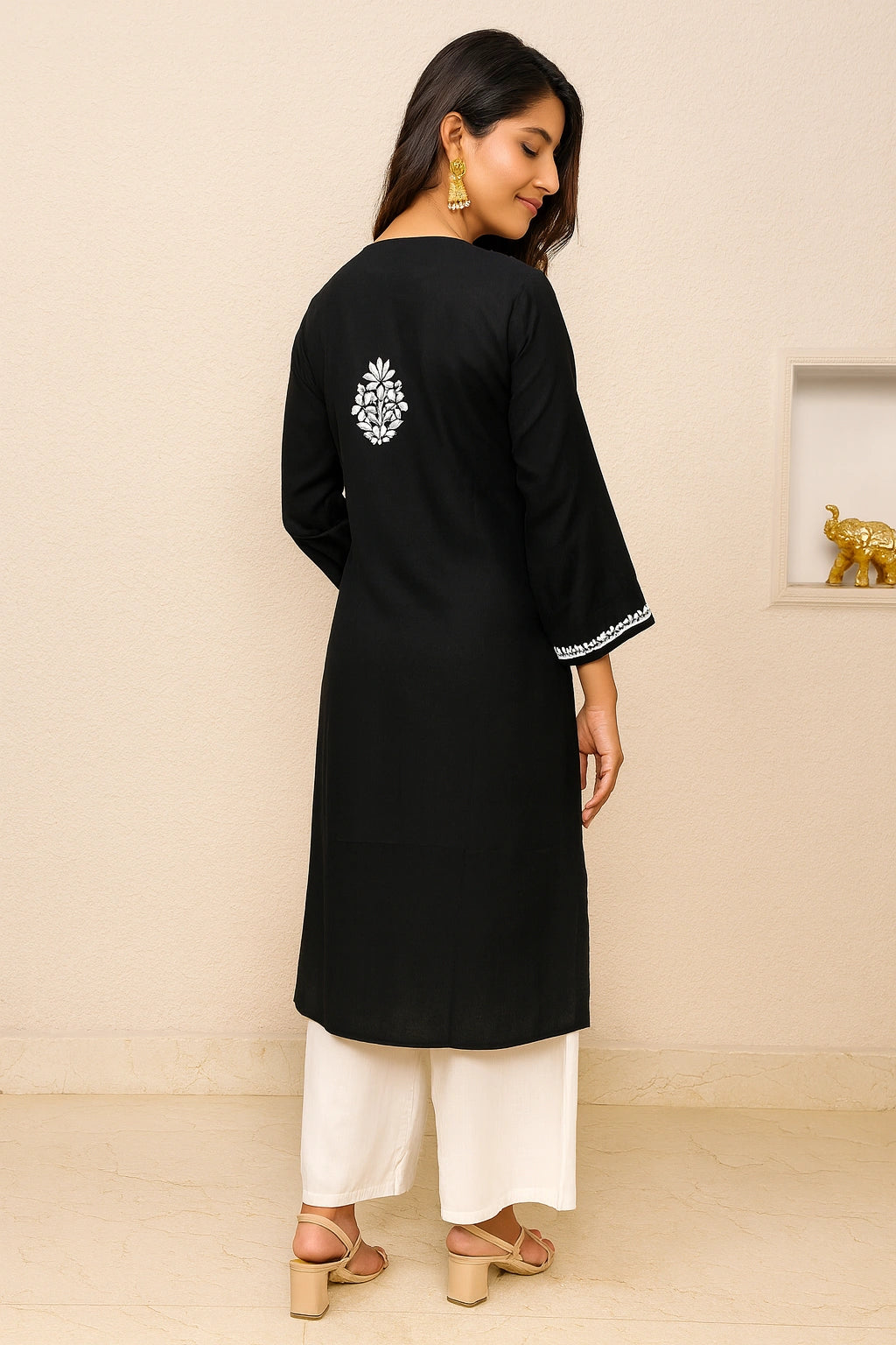 Woman wearing a black kurta with white embroidery and white pants against a beige background