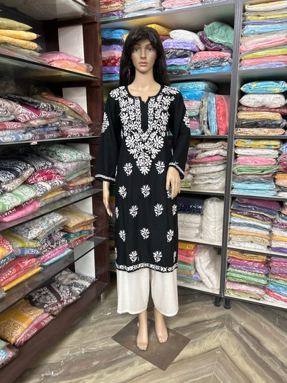 lucknowi chikankari Mannequin wearing a black and white patterned dress in front of shelves filled with colorful fabric.