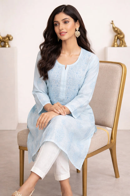 lucknowi chikankari Woman wearing a light blue kurta with white pants sitting on a chair.