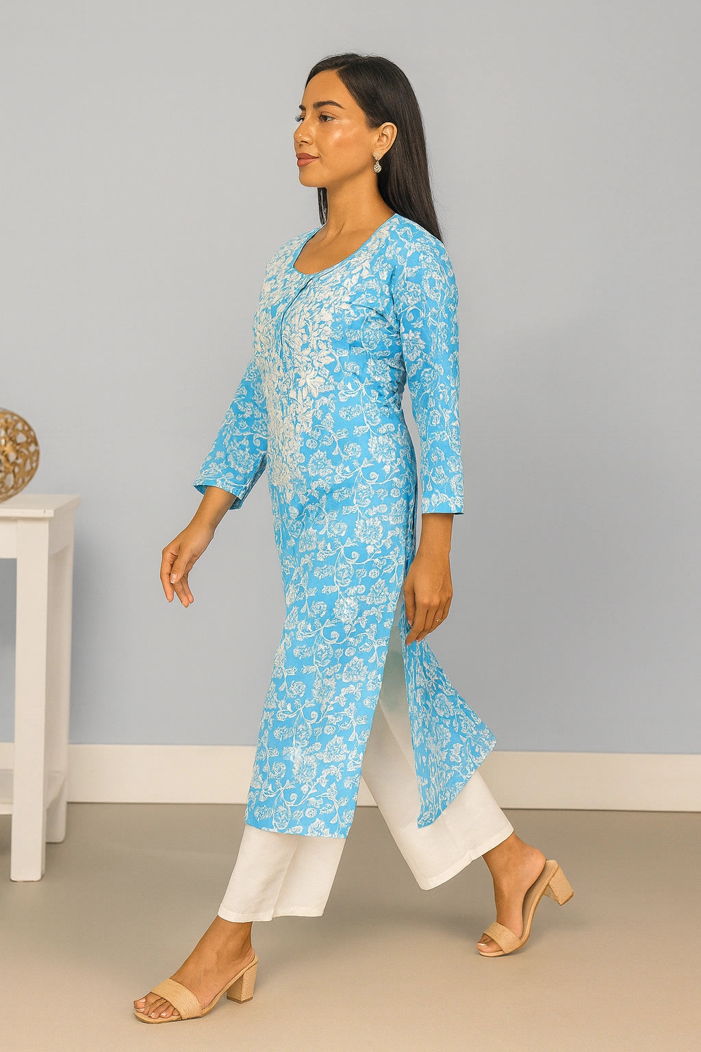 lucknowi chikankari Woman wearing a blue floral kurta with white pants against a gray wall.