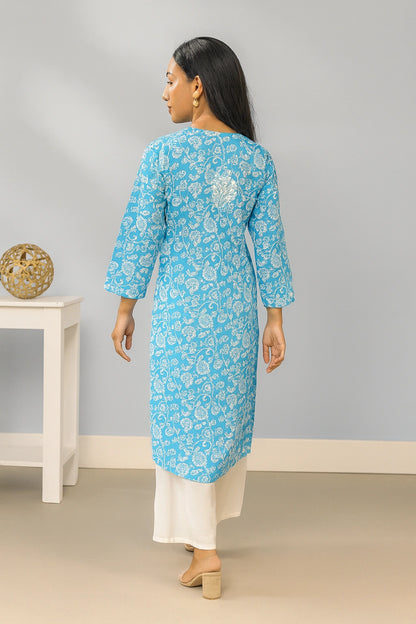 lucknowi chikankari Woman wearing a blue floral kurta with white pants against a gray wall.