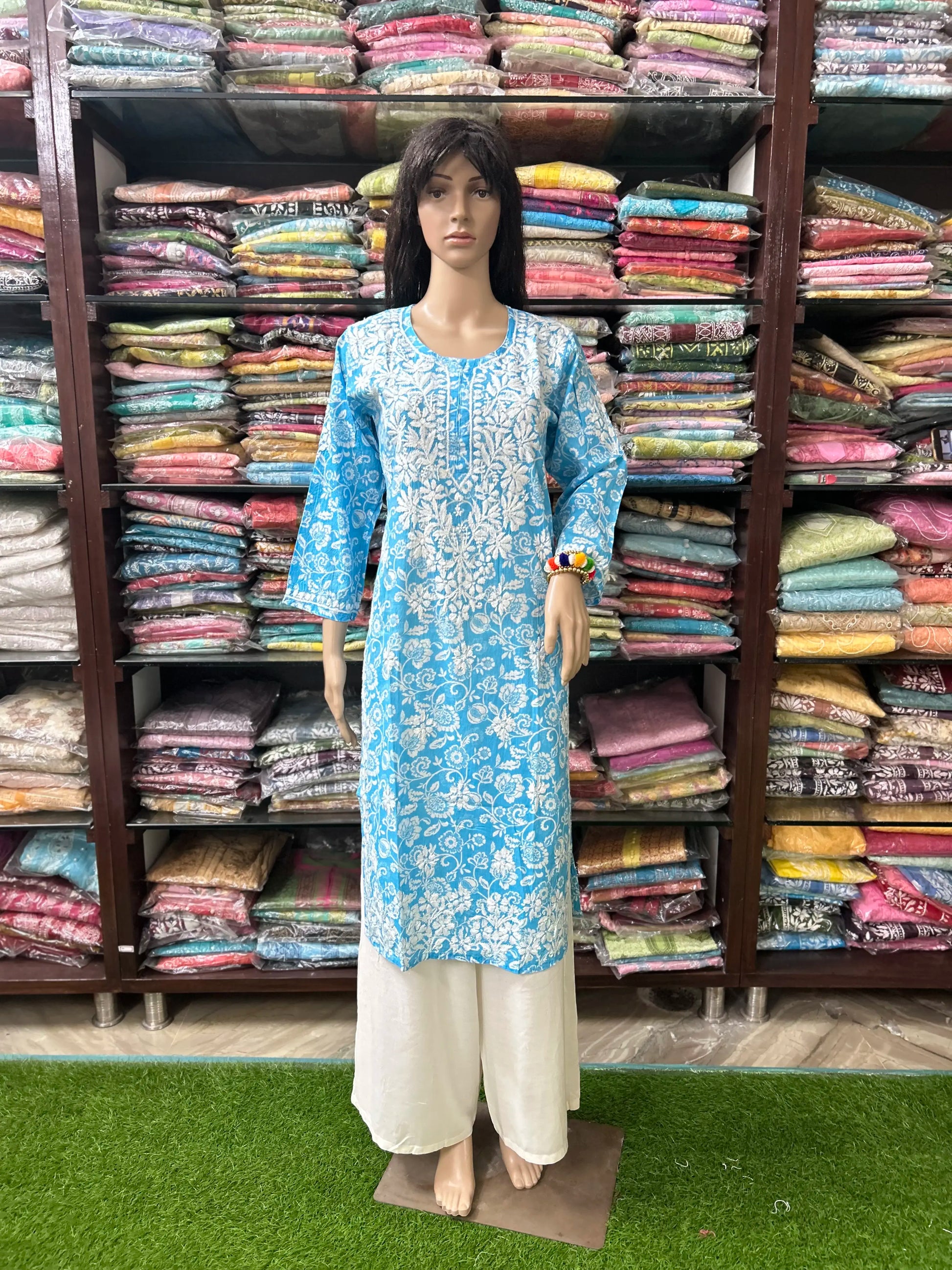 lucknowi chikankari Mannequin wearing a blue and white floral kurta with white pants in front of a colorful fabric background.