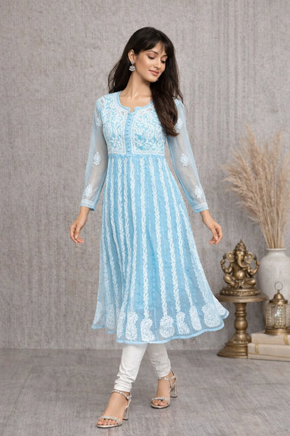 Woman wearing a light blue hand embroidered dress with white leggings and sandals, standing against a gray textured wall.