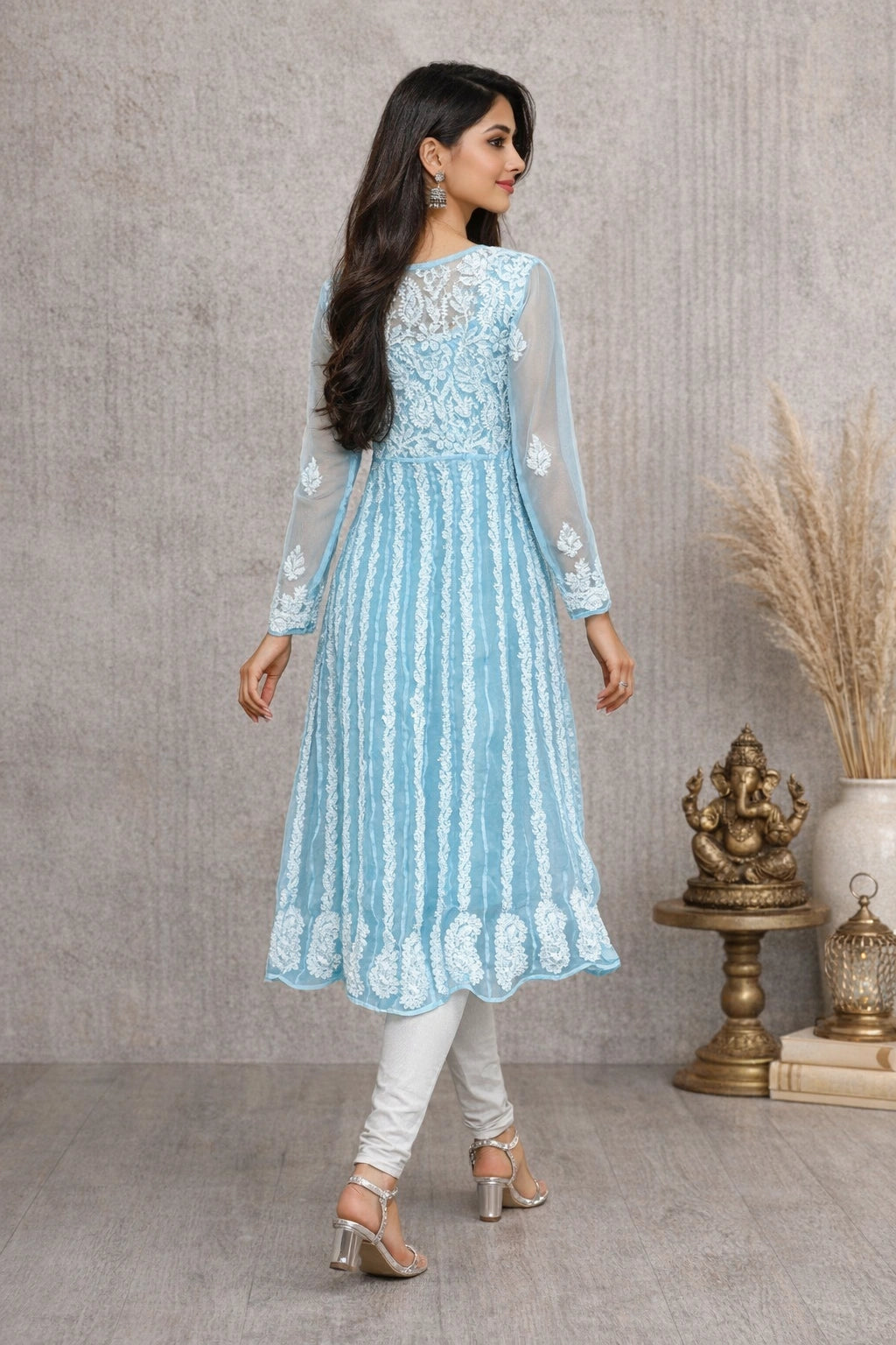 Woman wearing a light blue embroidered dress with white pants in a room setting.