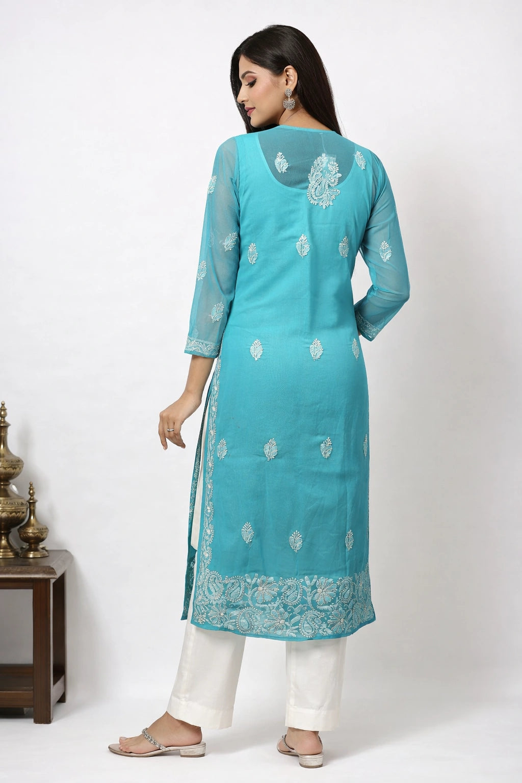 Woman wearing a turquoise embroidered kurta with white pants on a white background
