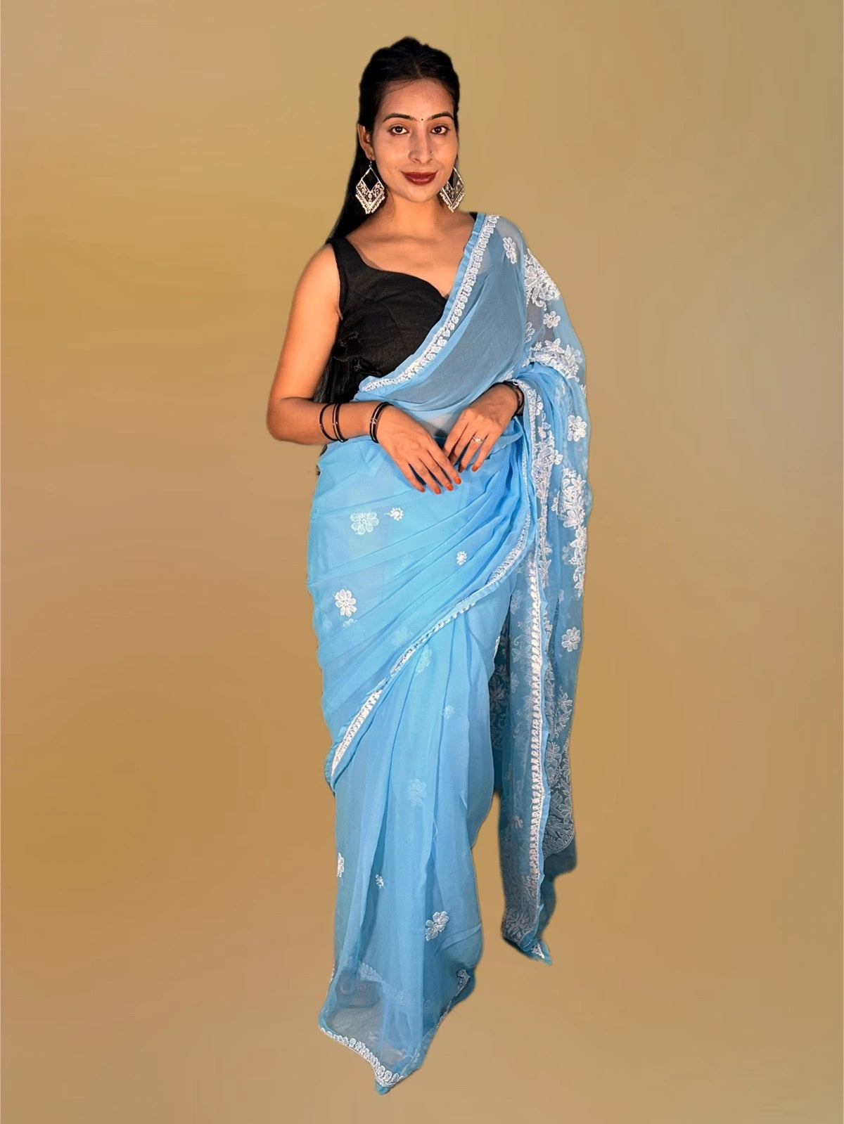Lucknowi chikankari A woman modeling a light blue saree with white floral patterns and a black sleeveless blouse, set against a solid beige background.