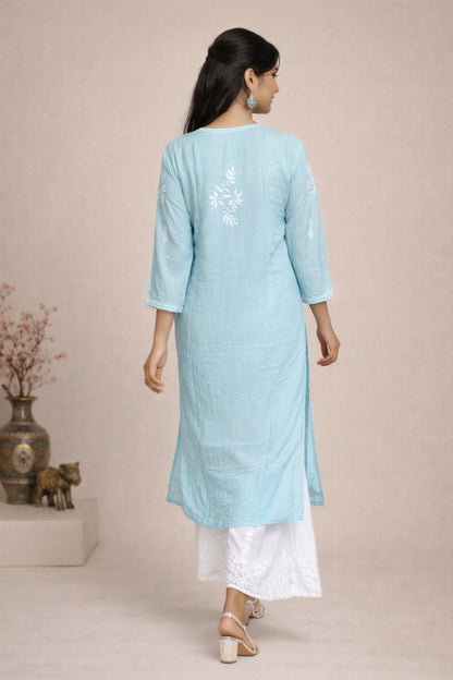 A woman is shown from the back wearing a light blue cotton kurta with white floral embroidery on the upper back, paired with white pants and beige sandals, set against a neutral beige background.
