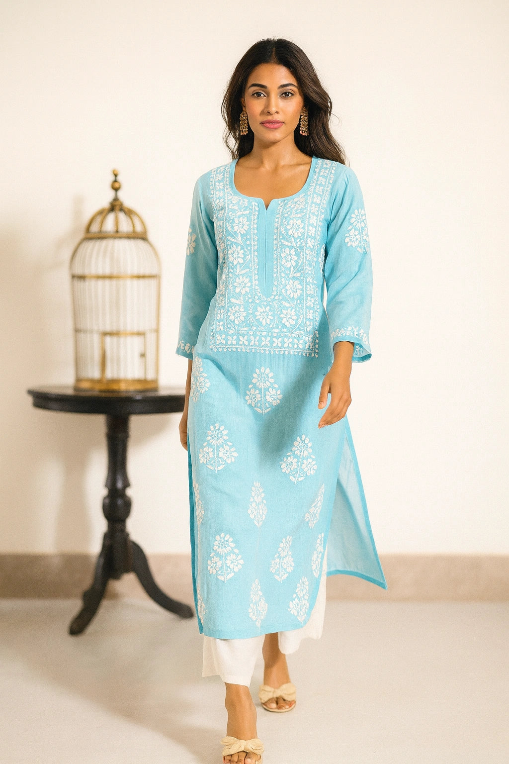 Woman wearing a light blue embroidered kurta with white pants in a minimalistic setting.