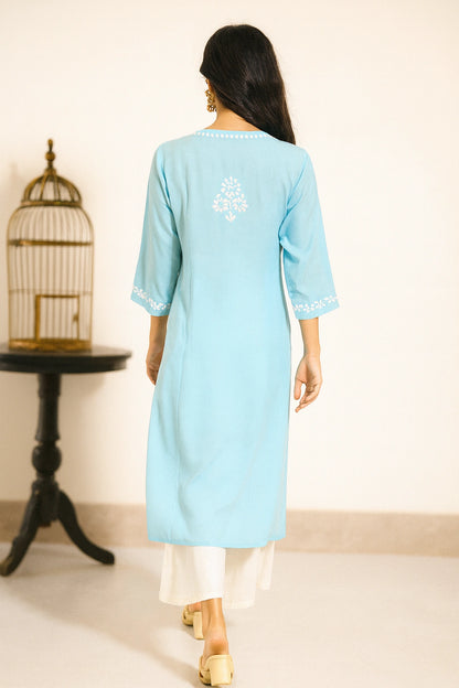 Woman wearing a light blue kurta with white embroidery in a minimal indoor setting.