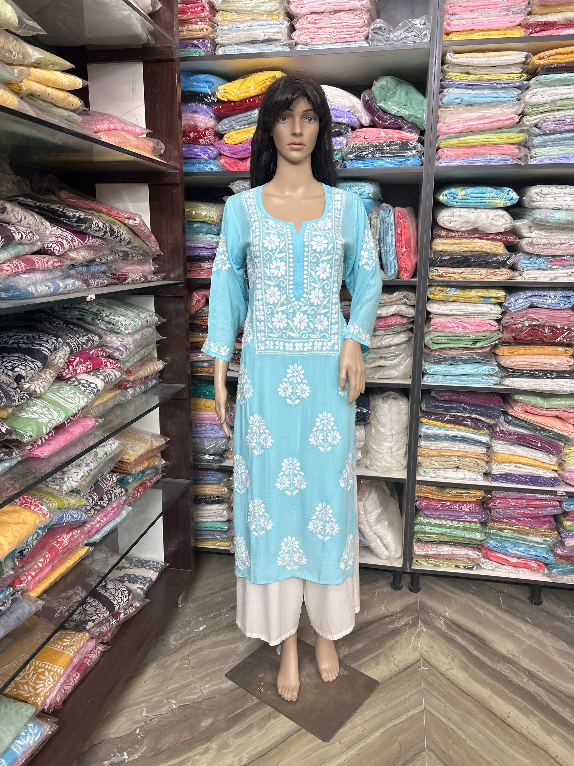 Mannequin wearing a blue embroidered dress in a fabric store with shelves of colorful fabrics.