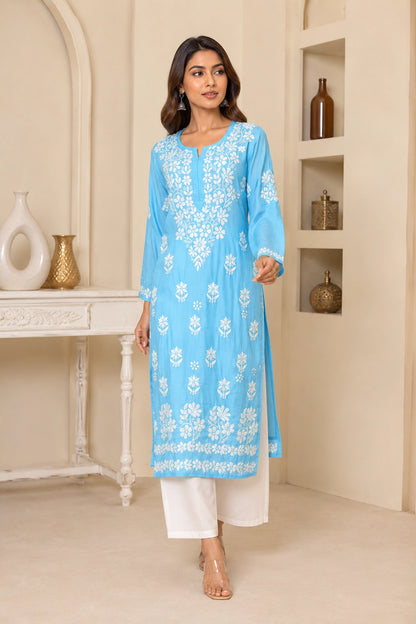 Woman wearing a light blue embroidered kurta with white pants in an indoor setting.