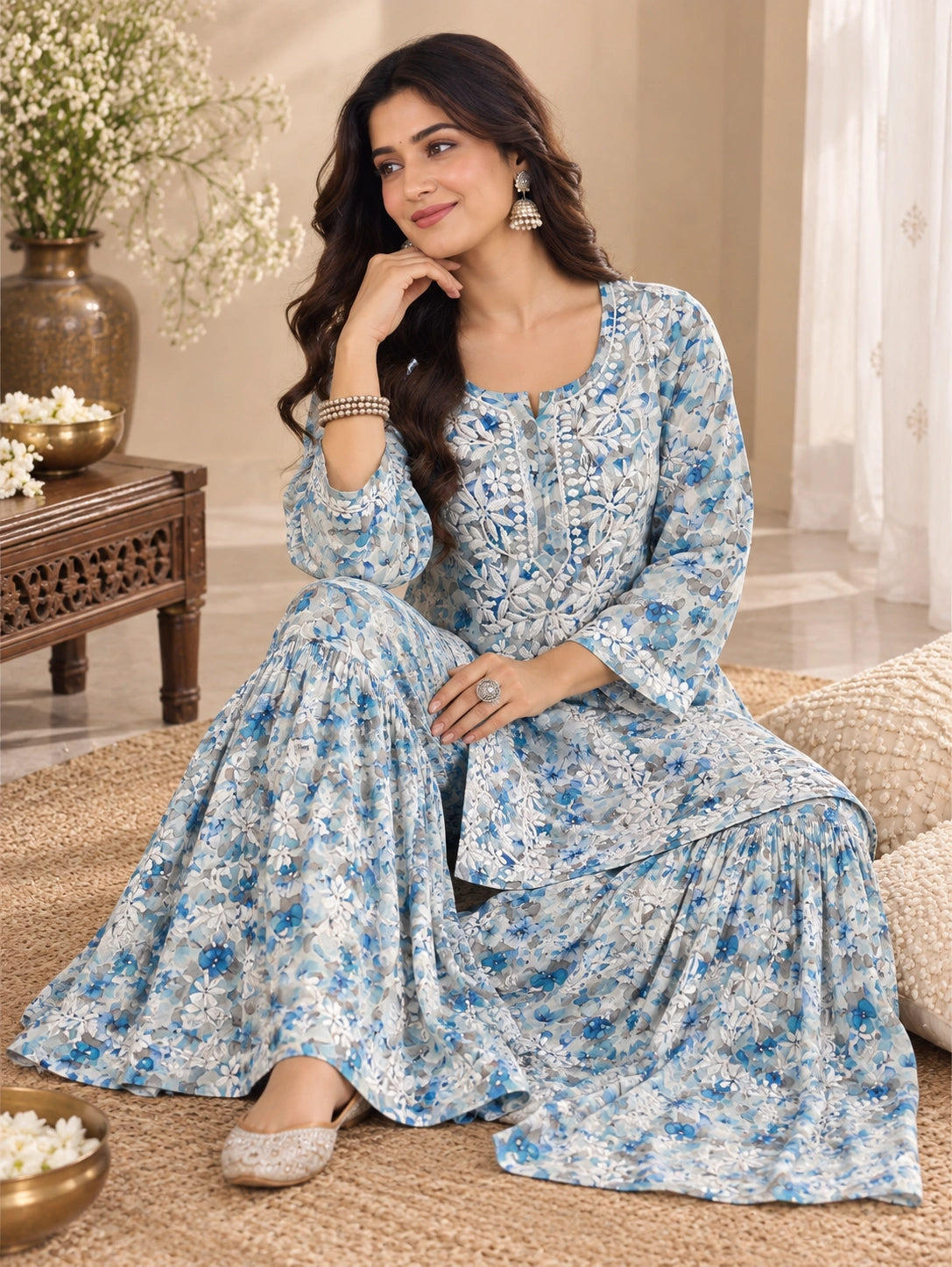 Lucknowi chikankari A woman models a blue and white floral printed kurta set while sitting on a woven rug in a warm, decorated room.
