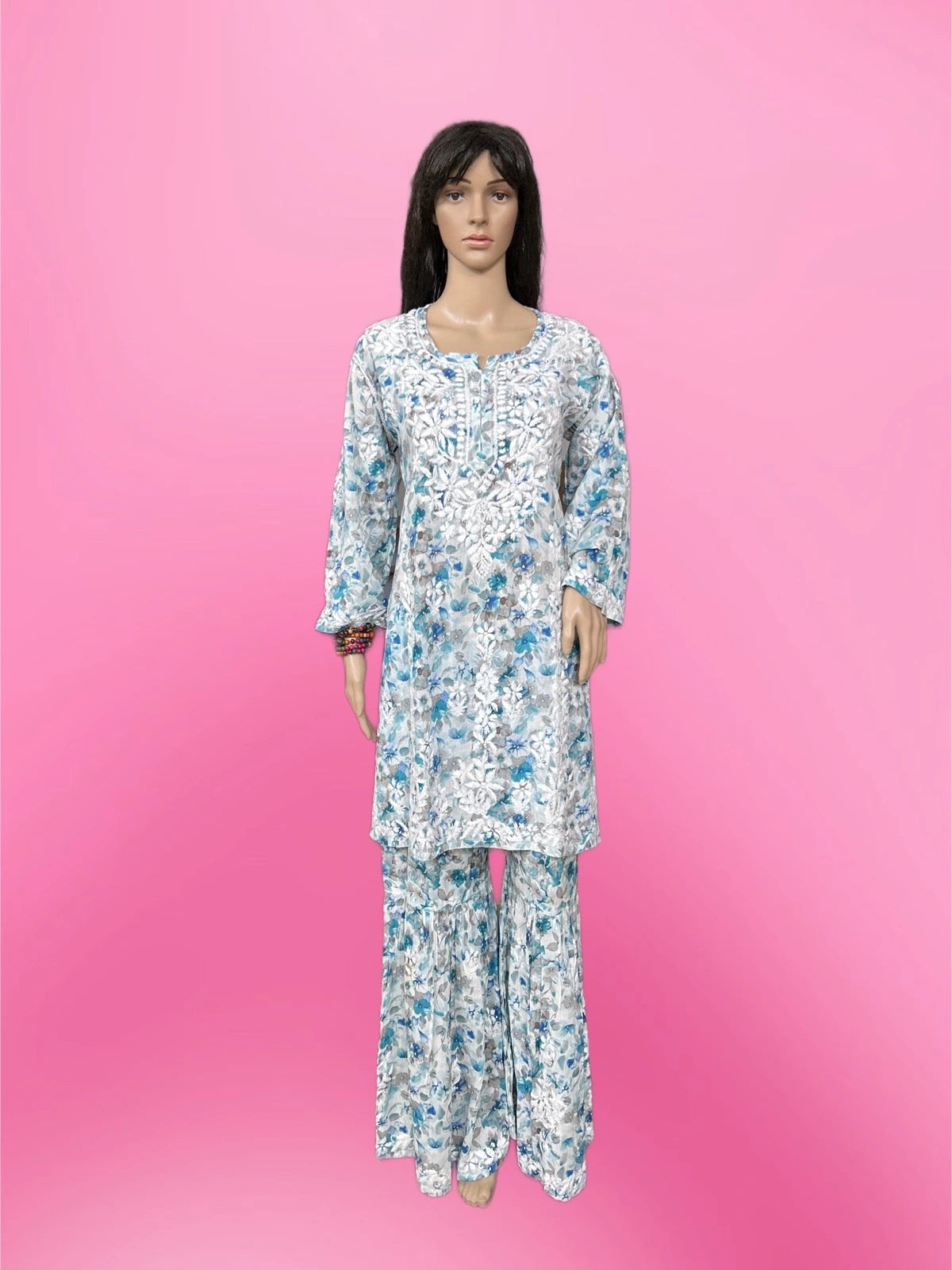 Lucknowi chikankari A mannequin wearing a long-sleeve white kurta and matching wide-leg pants set with a blue floral pattern, set against a solid pink background.