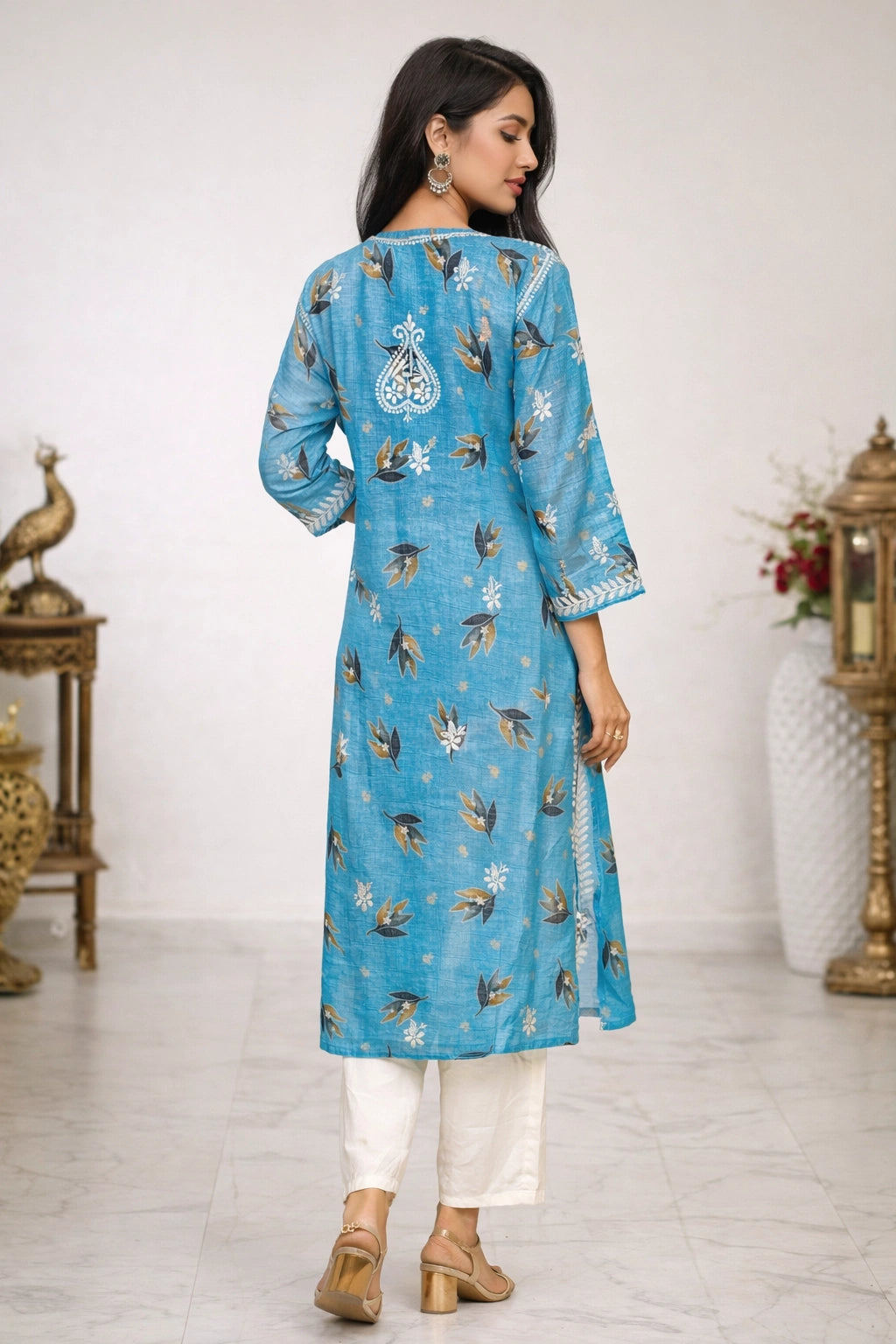 Woman wearing a blue embroidered kurta with white pants in a decorated room.