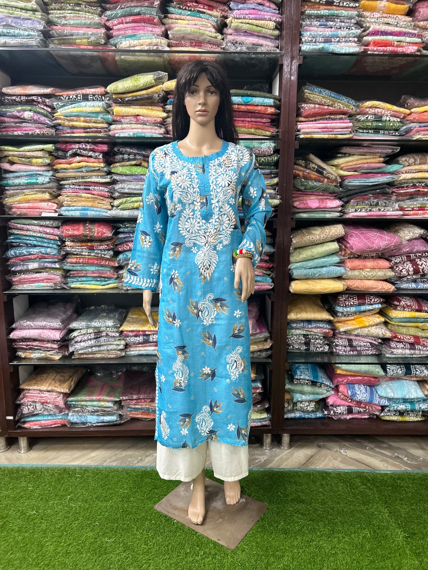 Mannequin wearing a blue embroidered dress in front of shelves filled with colorful fabrics.