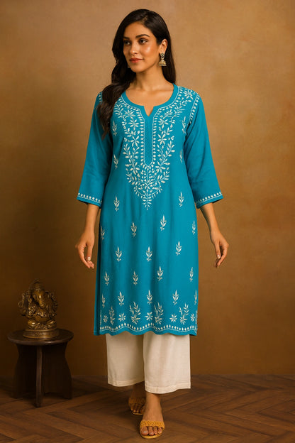 Woman wearing a blue embroidered kurta with white pants against a brown background