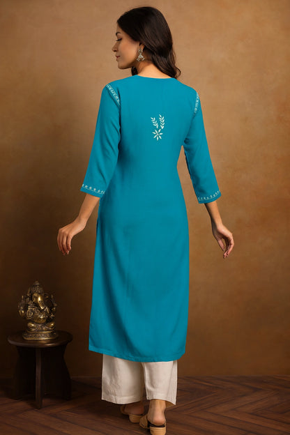 Woman wearing a blue embroidered kurta with white pants against a brown background