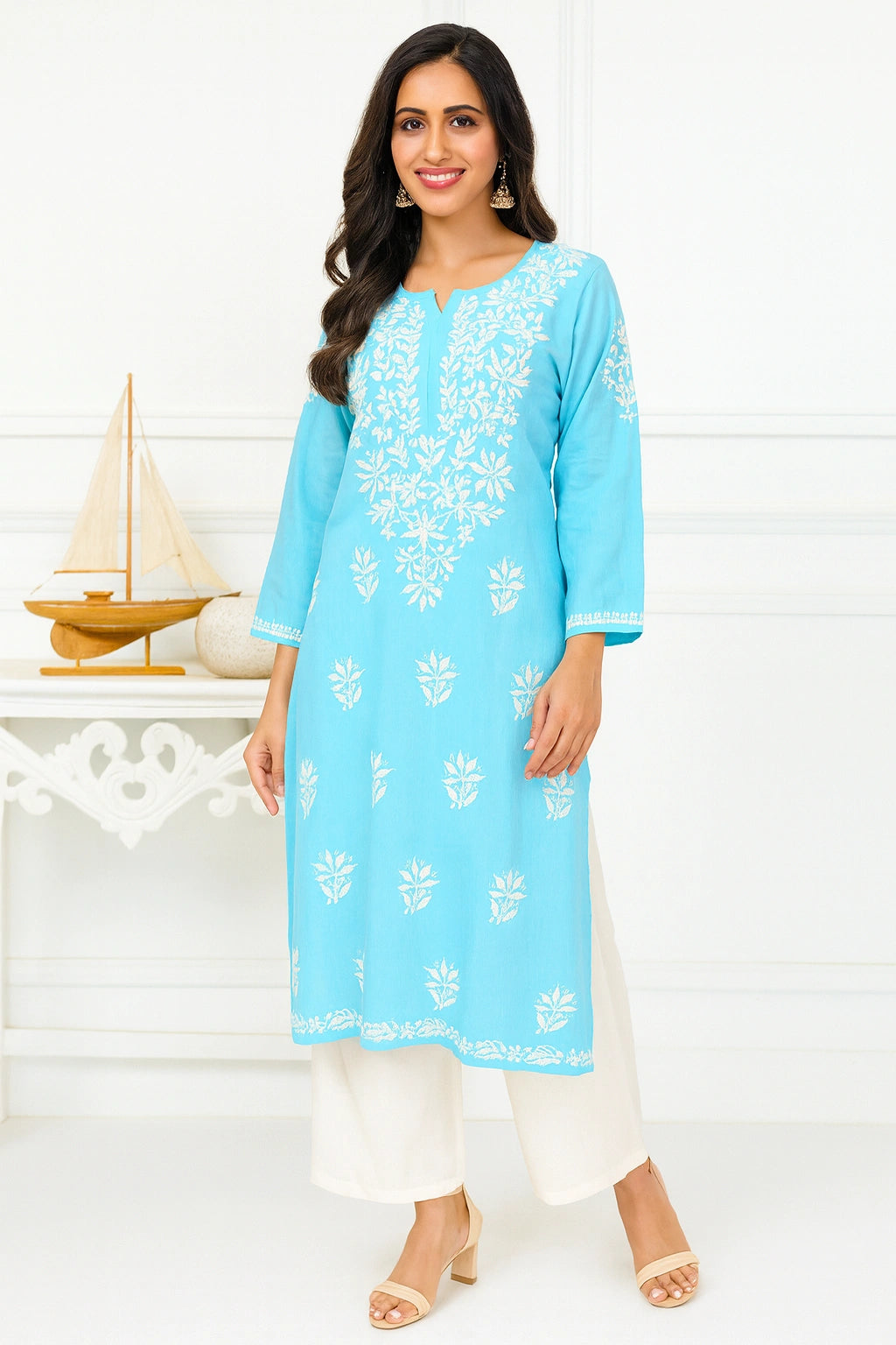 Woman wearing a light blue embroidered kurta with white pants on a white background