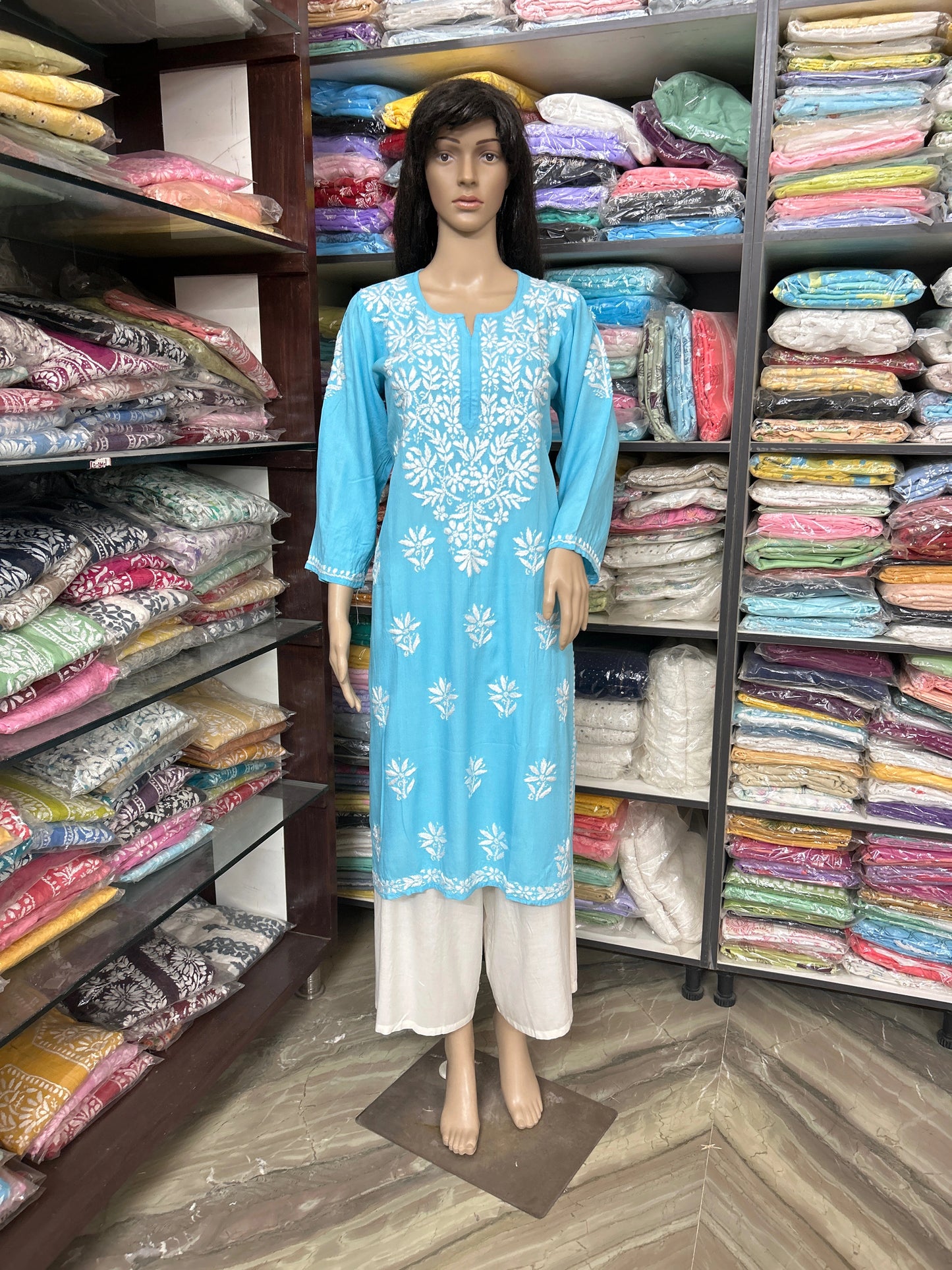 Mannequin wearing a blue embroidered kurta with white pants in a fabric store.