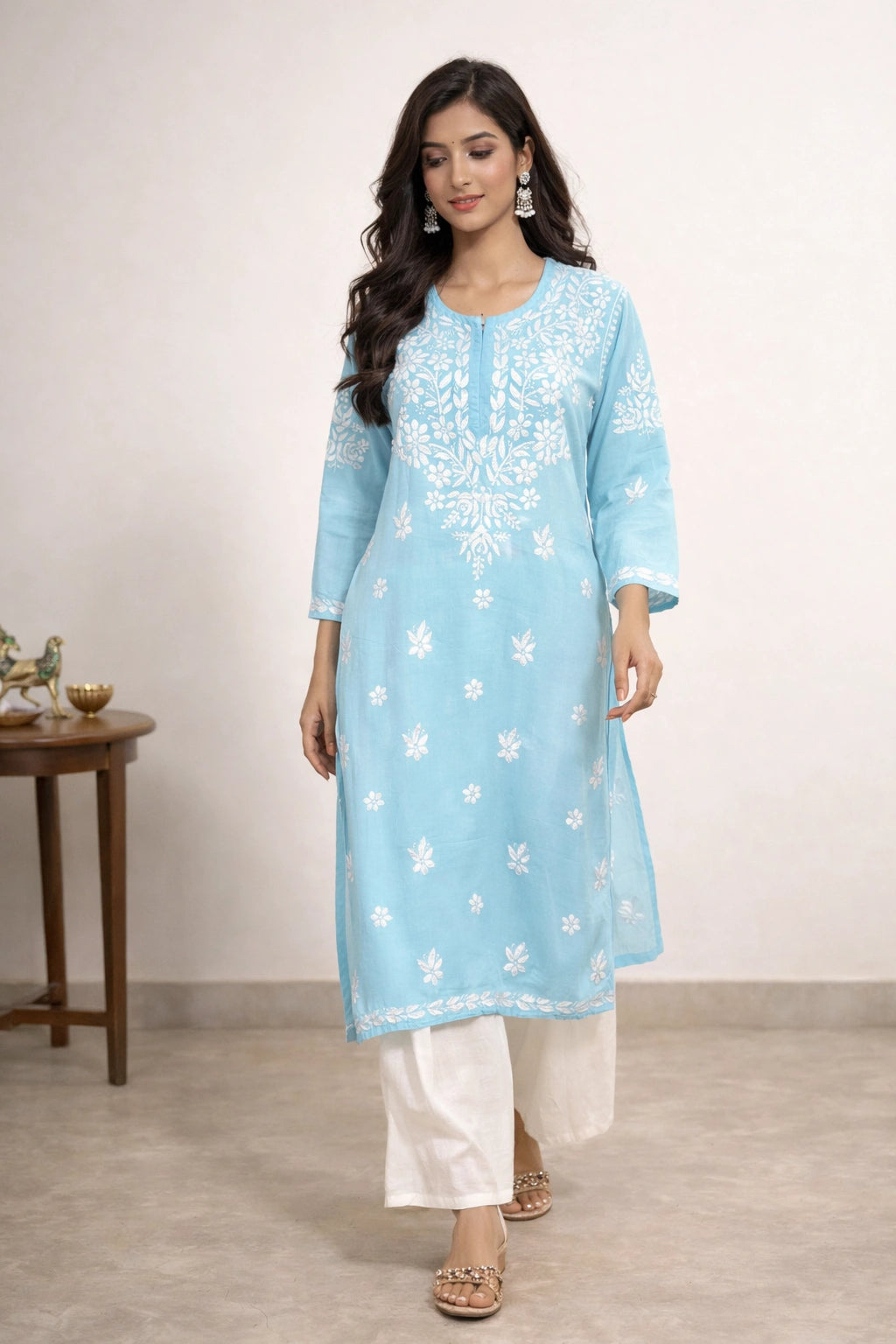 Woman wearing a light blue embroidered kurta with white pants against a plain background