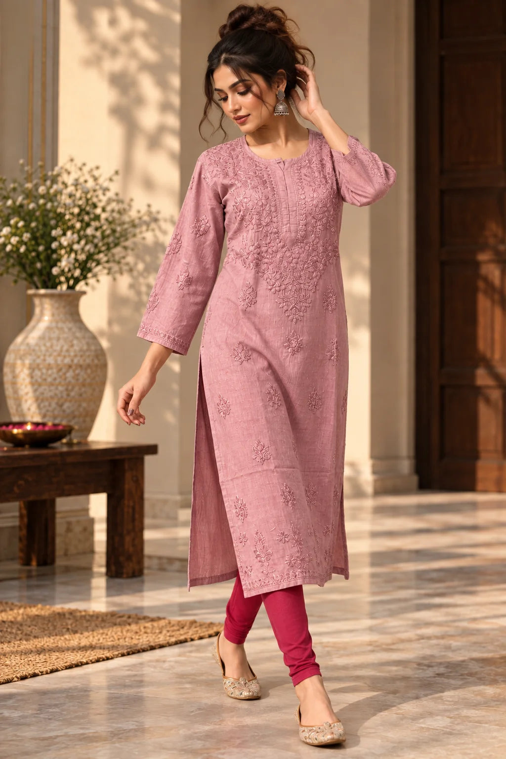 A woman models a dusty pink embroidered kurta with three-quarter sleeves, paired with magenta leggings and beige embellished flat shoes, standing in a sunlit indoor courtyard setting.