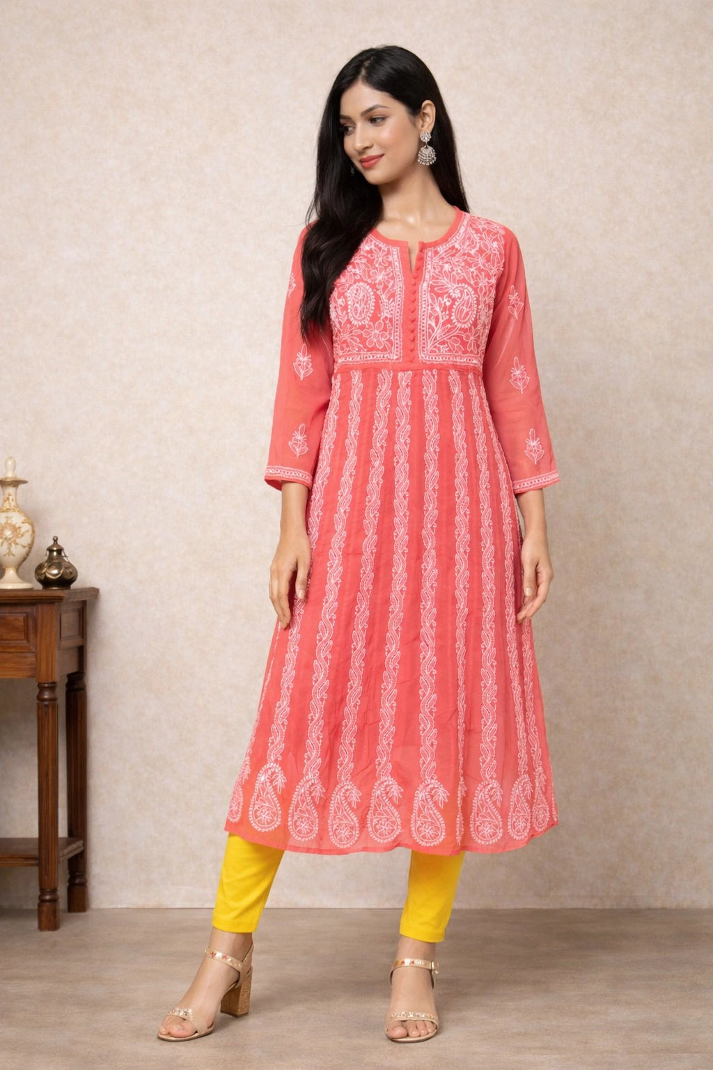 Woman wearing a pink embroidered kurta with yellow pants against a beige wall.
