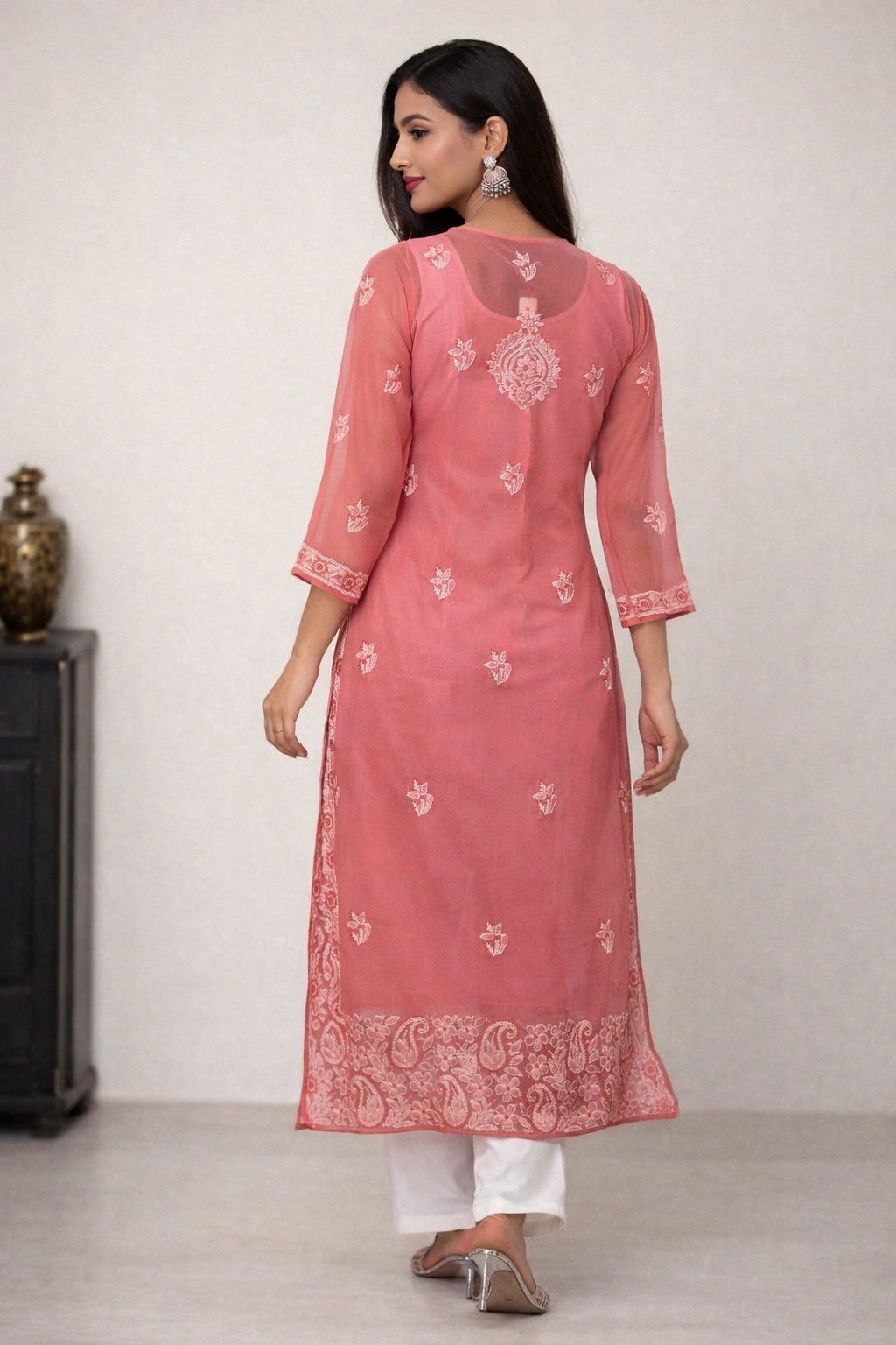 Woman wearing a pink embroidered kurta with white pants against a plain background