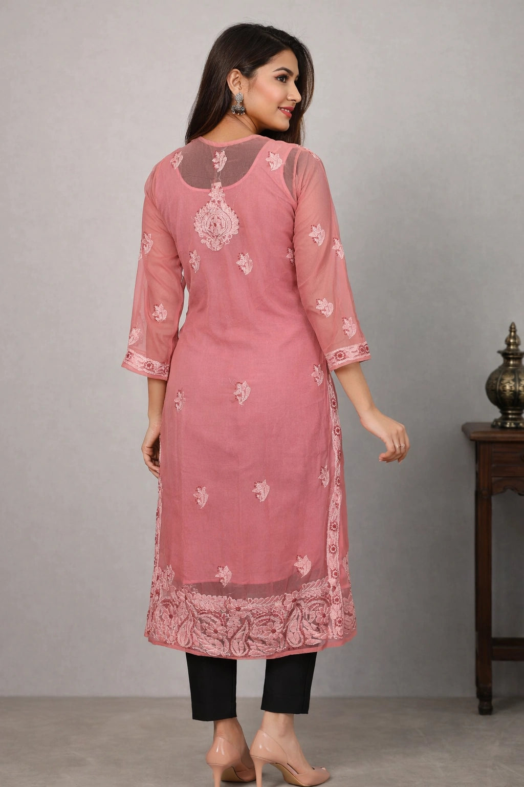 Woman wearing a pink embroidered kurta with black pants against a gray background