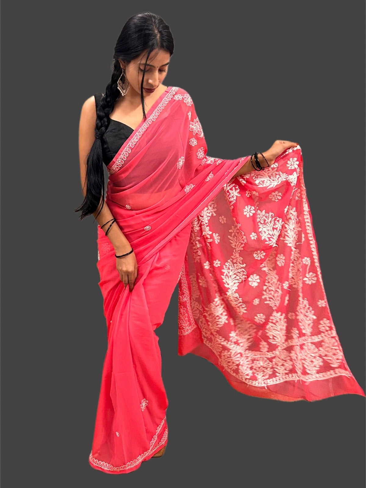 Lucknowi Chikankari A woman modeling a bright pink saree with white floral patterns and a black sleeveless blouse, posed against a solid dark gray background.