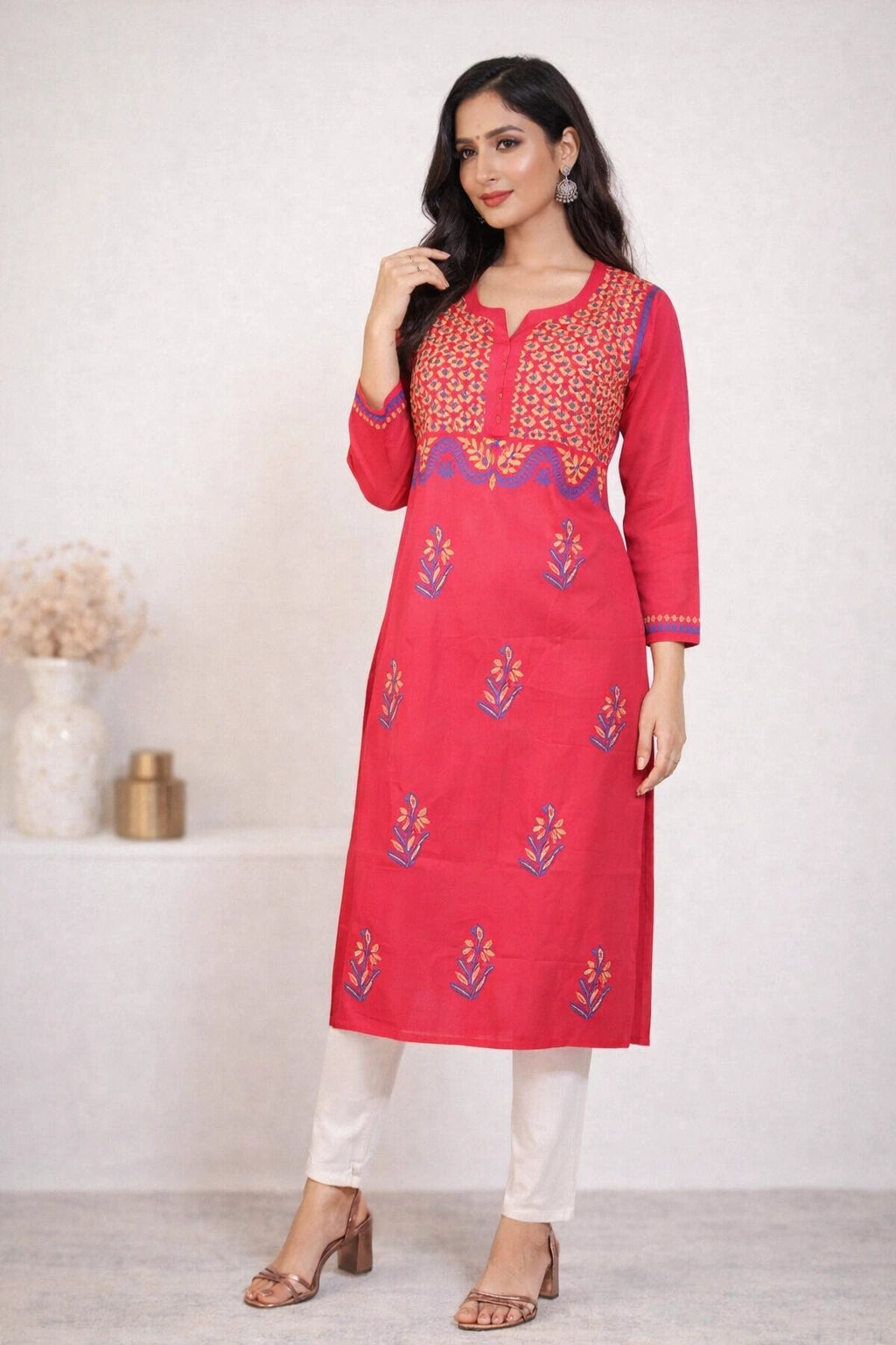 Woman wearing a red embroidered kurta with white pants against a white background