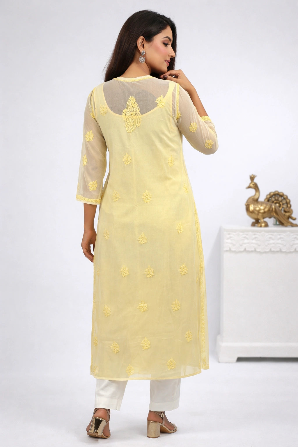 Woman wearing a yellow embroidered kurta with white pants on a white background