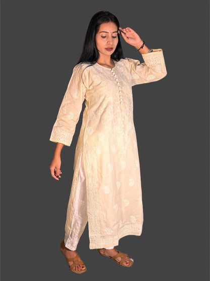 A woman modeling a long cream-colored embroidered tunic or kurta with three-quarter sleeves and lace trim, shown against a solid dark gray background.