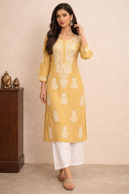 Woman wearing a yellow embroidered kurta with white pants against a beige background