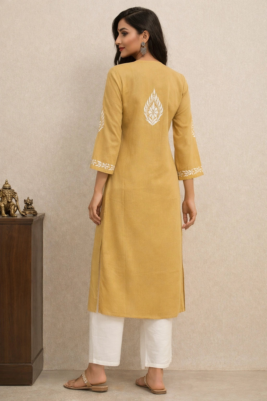 Woman wearing a mustard yellow kurta with white embroidery against a beige wall.