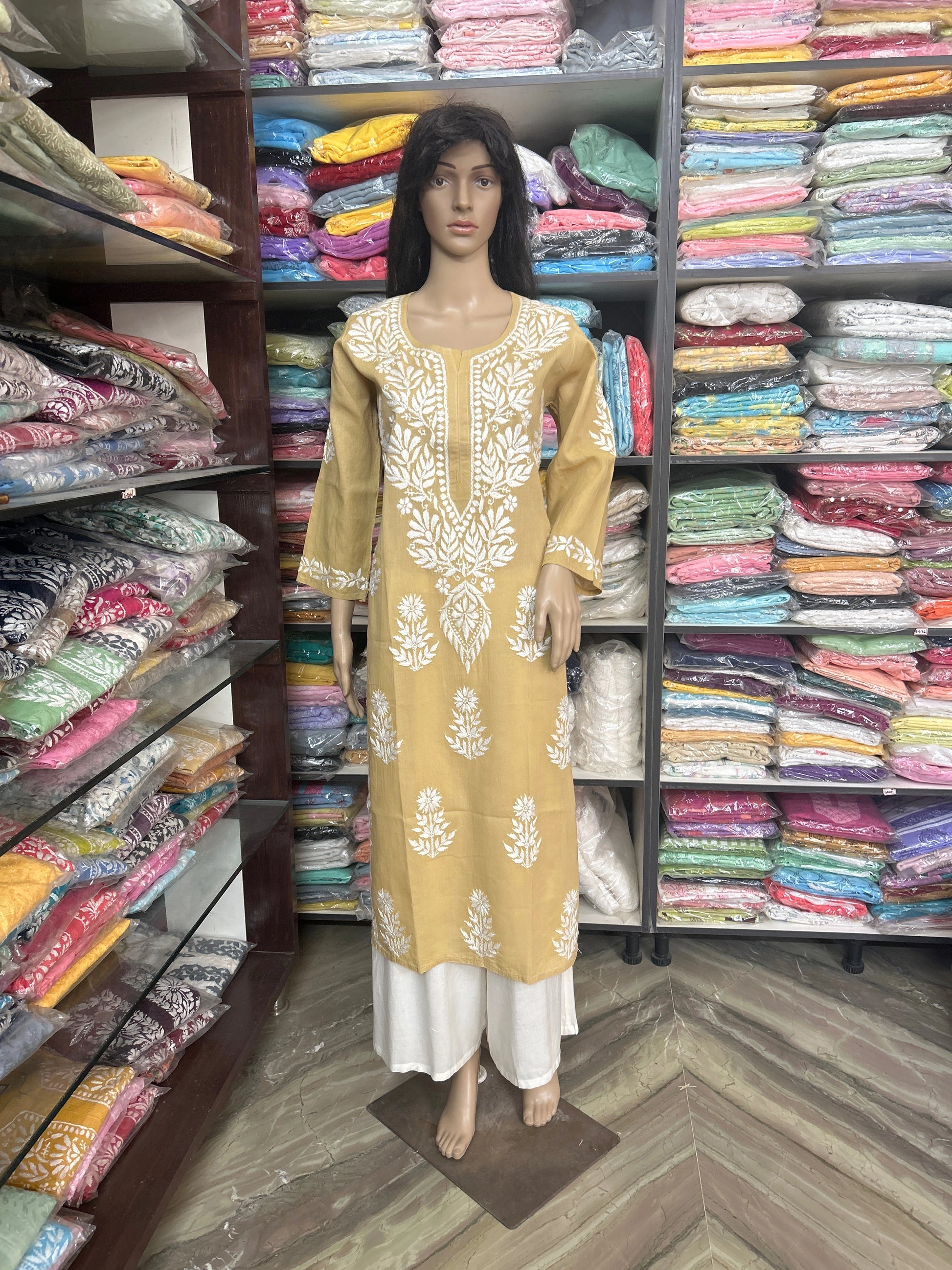 Mannequin wearing a yellow and white embroidered outfit in a fabric store.