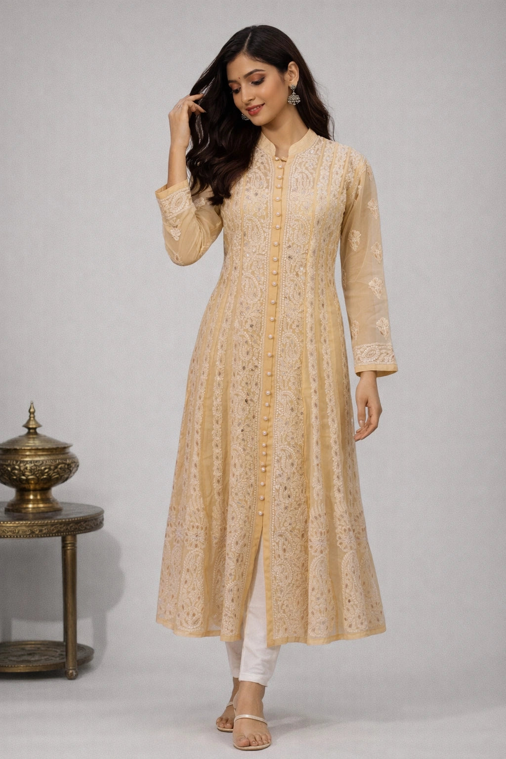 Woman wearing a beige embroidered kurta with white pants against a gray background