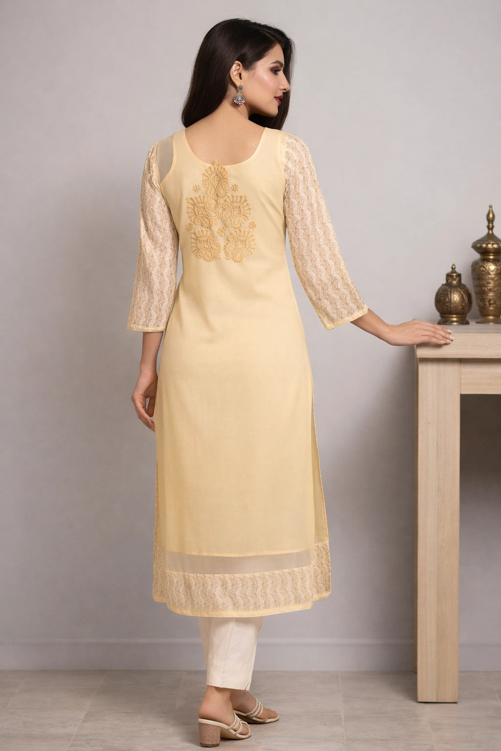 Woman wearing a beige embroidered kurta with white pants against a plain background