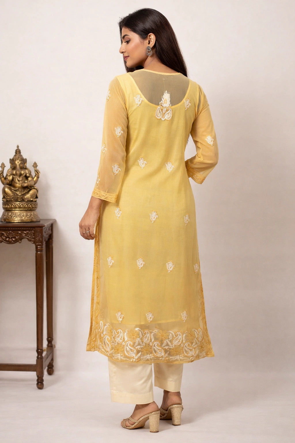 Woman wearing a yellow embroidered kurta with white pants against a neutral background