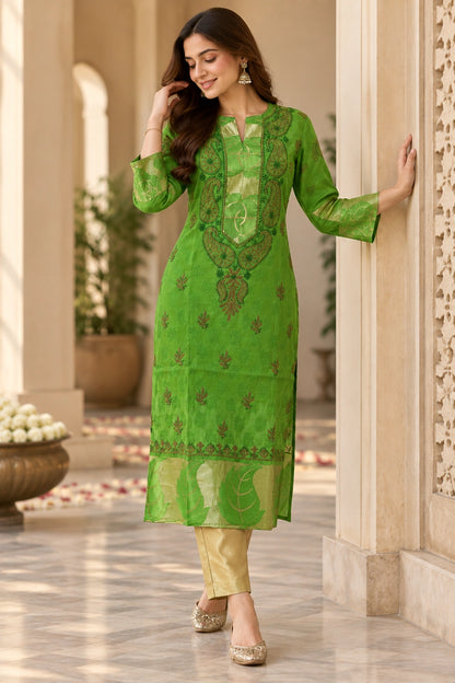 A woman models a bright green embroidered kurta with matching pants in a traditional architectural corridor with beige pillars and tiled floors.