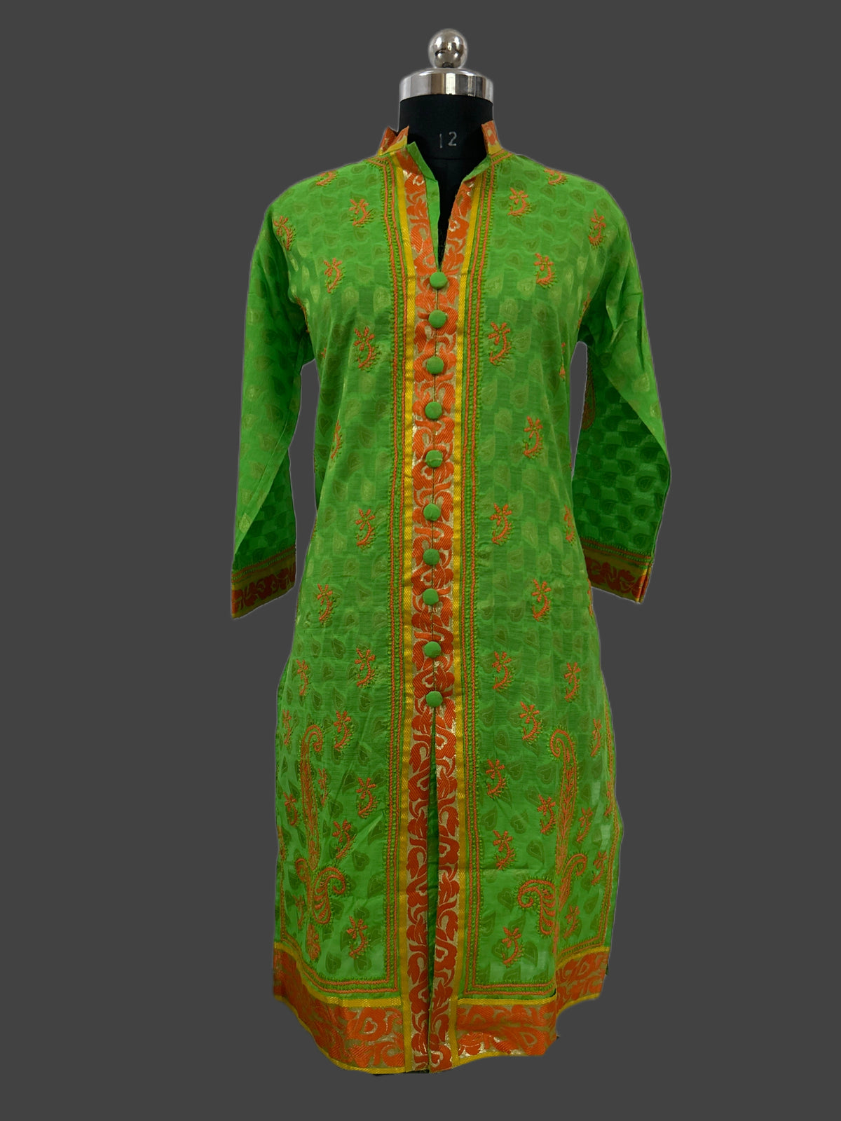Lucknowi chikankari A green long kurta with orange and gold patterns, displayed on a black mannequin against a dark gray background.