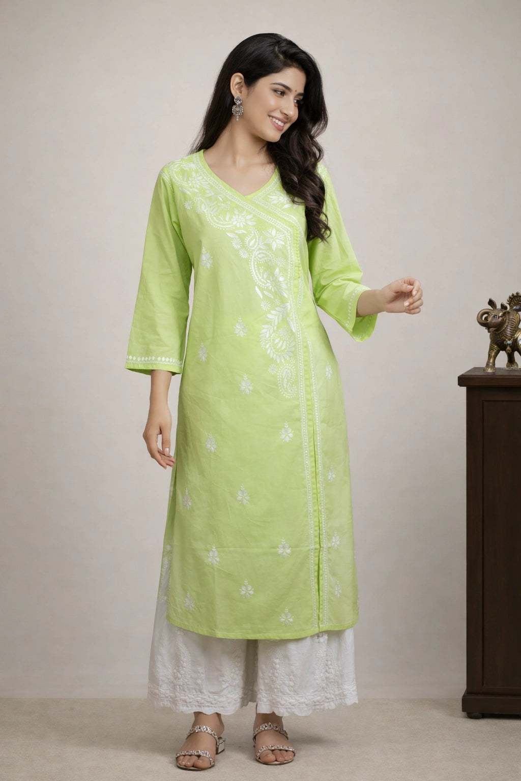 A woman modeling a light green kurta with white embroidery, paired with white pants, standing in front of a neutral beige background.