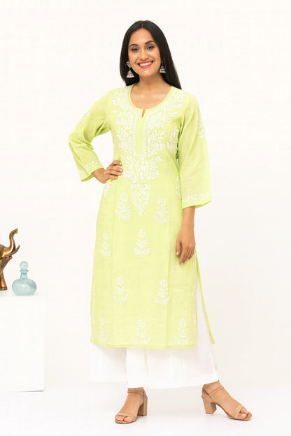 A woman modeling a light yellow-green kurta with white floral embroidery, paired with white pants and beige heeled sandals, set against a plain white studio background.