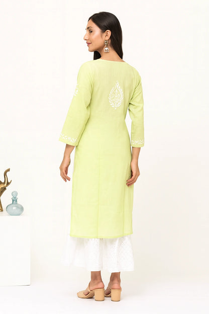 Lucknow chikankari A woman modeling a light yellow-green kurta from the back, featuring white embroidery on the back and cuffs, paired with a white flared skirt and beige block-heel sandals against a white studio background.