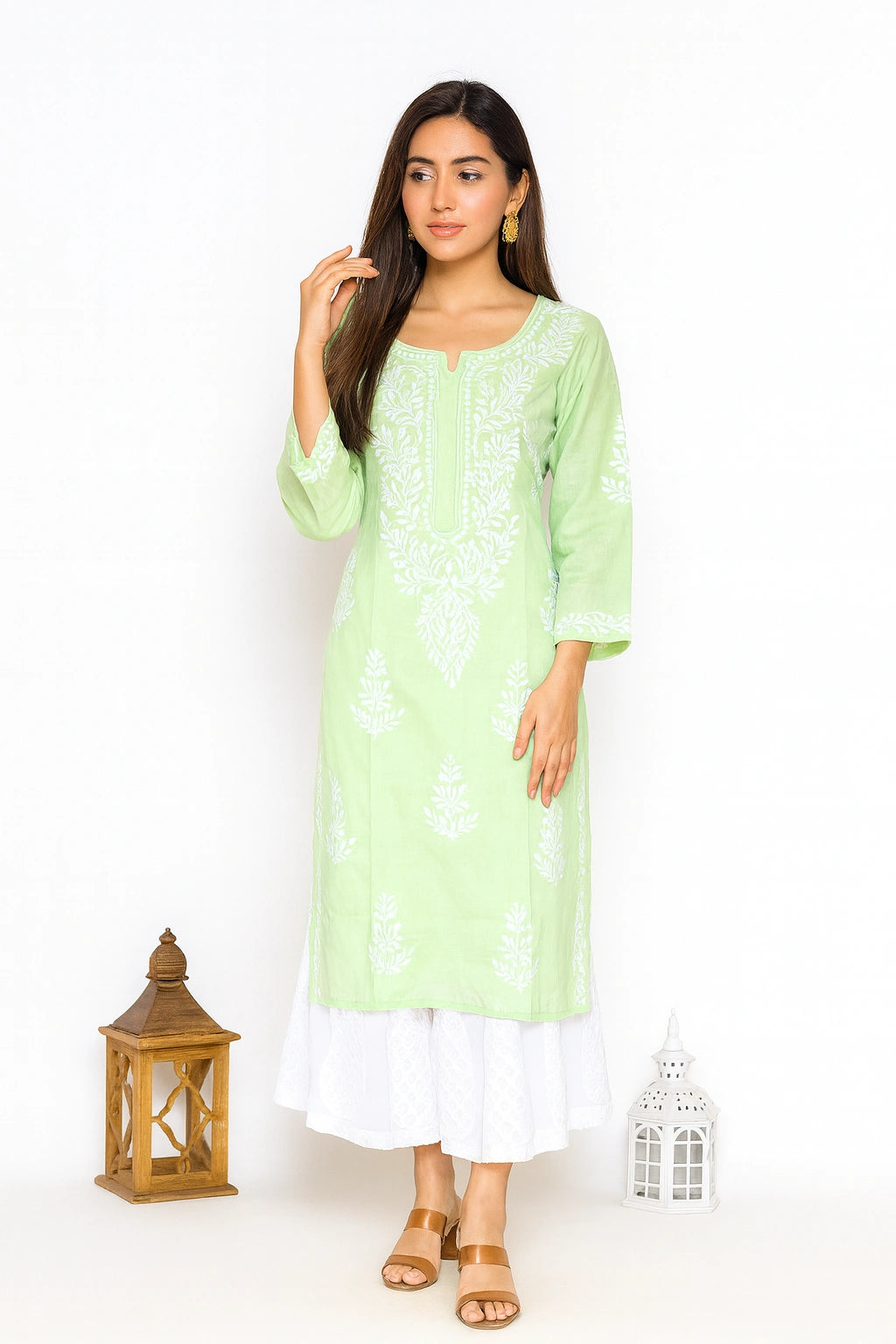 lucnowi chikankari A woman modeling a light green kurta with white floral embroidery, paired with a white layered skirt and tan sandals, set against a plain white background with decorative lanterns.