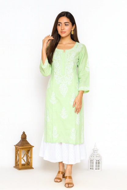 lucnowi chikankari A woman modeling a light green kurta with white floral embroidery, paired with a white layered skirt and tan sandals, set against a plain white background with decorative lanterns.